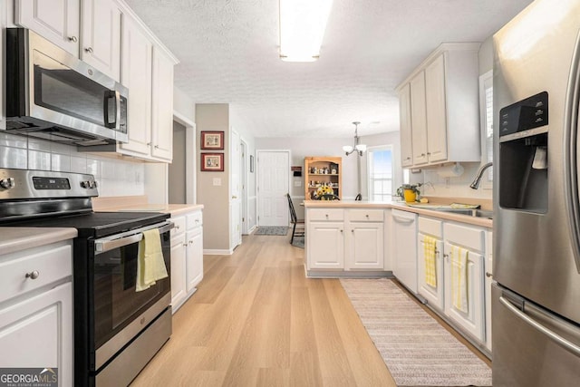 kitchen featuring a peninsula, a sink, stainless steel appliances, light wood-type flooring, and a chandelier