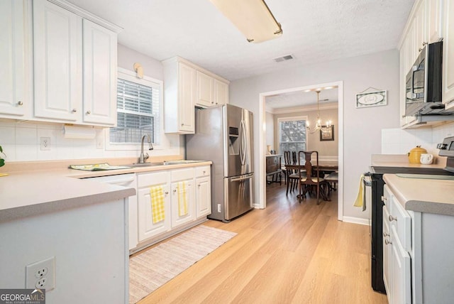 kitchen with visible vents, light wood-style flooring, a sink, decorative backsplash, and appliances with stainless steel finishes