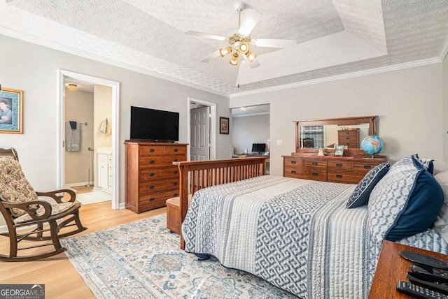 bedroom with a tray ceiling, a textured ceiling, light wood-style flooring, and ornamental molding