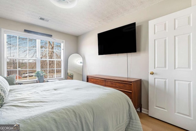 bedroom featuring light wood-style flooring, visible vents, and a textured ceiling