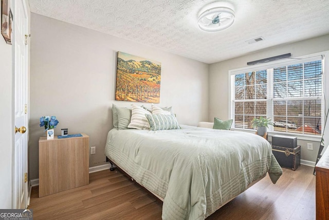 bedroom with visible vents, baseboards, a textured ceiling, and wood finished floors