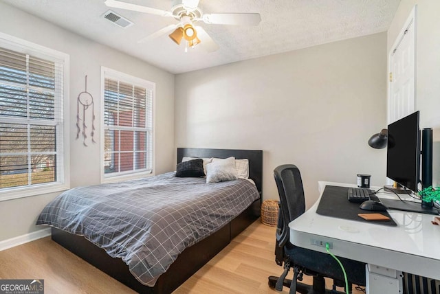 bedroom with visible vents, ceiling fan, baseboards, wood finished floors, and a textured ceiling