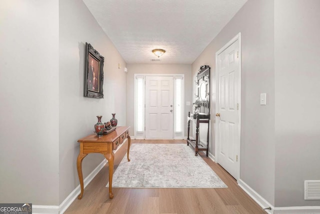 foyer entrance featuring visible vents, a textured ceiling, baseboards, and wood finished floors