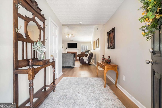 corridor with a textured ceiling, baseboards, and wood finished floors