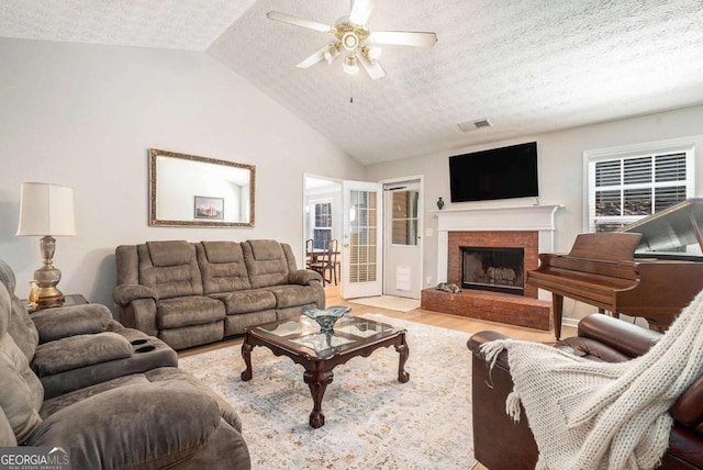 living area with lofted ceiling, a textured ceiling, light wood-style flooring, and a ceiling fan