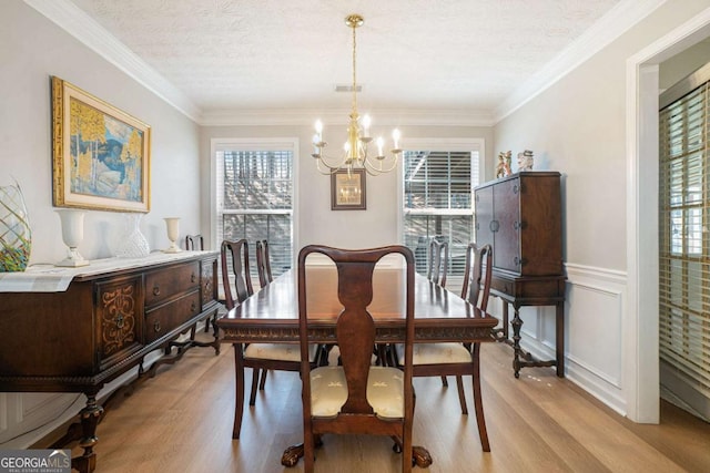 dining space with wainscoting, a notable chandelier, a healthy amount of sunlight, and light wood-style flooring