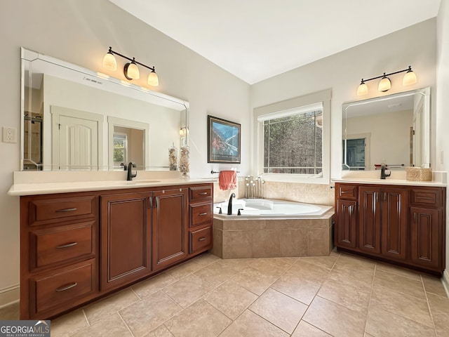 bathroom with tile patterned flooring, two vanities, a garden tub, and a sink