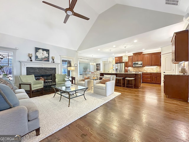 living area featuring a glass covered fireplace, plenty of natural light, ceiling fan, and wood finished floors