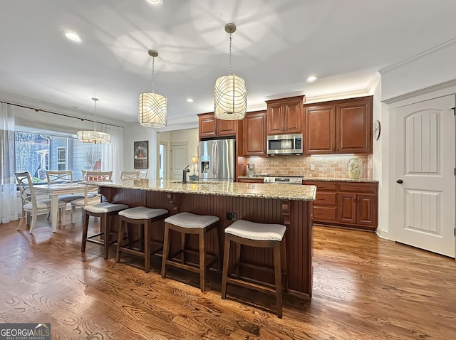 kitchen featuring a breakfast bar area, a kitchen island with sink, dark wood-style flooring, stainless steel appliances, and backsplash