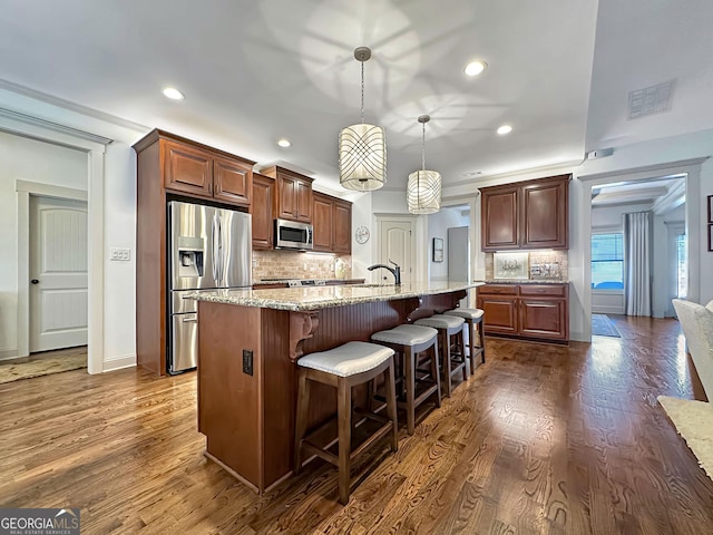 kitchen with a breakfast bar, a kitchen island with sink, tasteful backsplash, stainless steel appliances, and light stone countertops