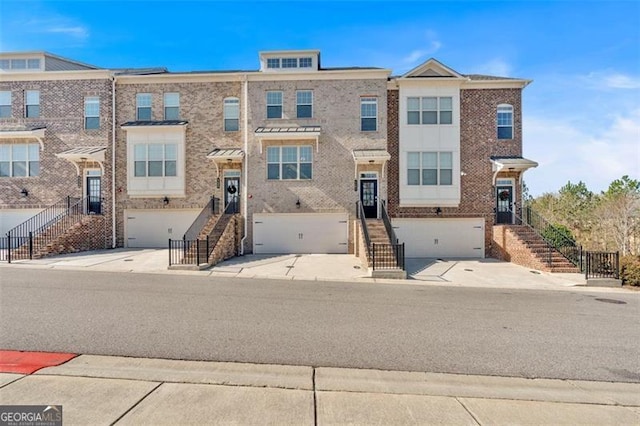 townhome / multi-family property with concrete driveway, stairway, brick siding, and a garage