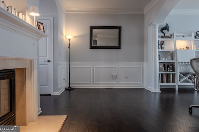 living area with dark wood finished floors, decorative columns, a wainscoted wall, and ornamental molding