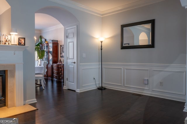 interior space with a wainscoted wall, arched walkways, dark wood finished floors, and ornamental molding
