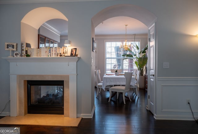 dining space featuring a notable chandelier, ornamental molding, a decorative wall, a multi sided fireplace, and dark wood-style flooring