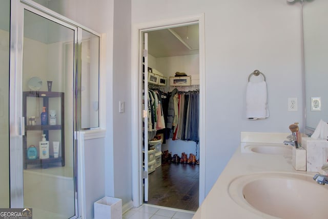 bathroom featuring a walk in closet, double vanity, a stall shower, and a sink
