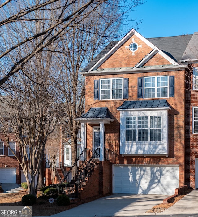 view of front facade featuring a standing seam roof, an attached garage, brick siding, and driveway