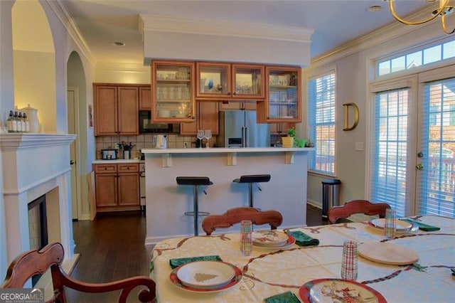 kitchen with crown molding, black microwave, stainless steel fridge with ice dispenser, a breakfast bar area, and brown cabinets