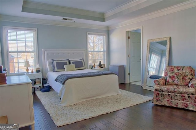bedroom with a tray ceiling, dark wood-type flooring, visible vents, and crown molding