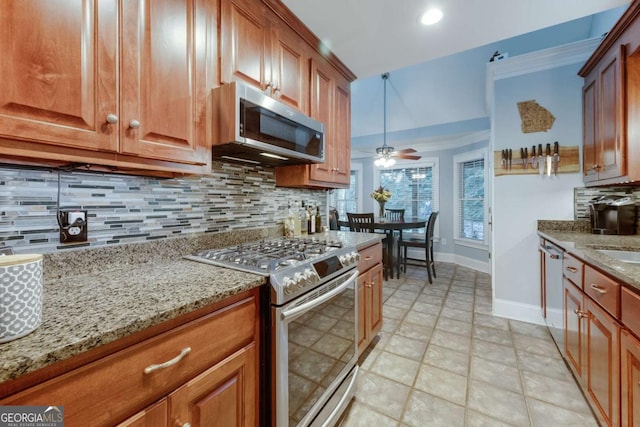 kitchen with brown cabinetry, light stone countertops, a ceiling fan, appliances with stainless steel finishes, and backsplash