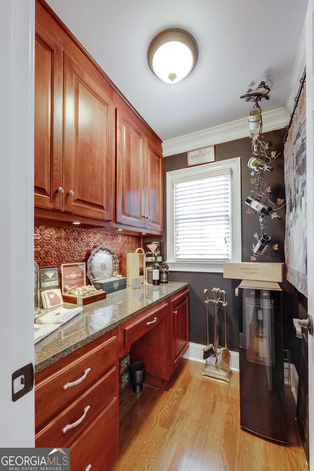 kitchen featuring light wood finished floors, backsplash, ornamental molding, brown cabinetry, and stone countertops