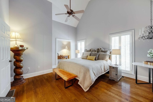 bedroom featuring wood finished floors, baseboards, visible vents, high vaulted ceiling, and ceiling fan with notable chandelier