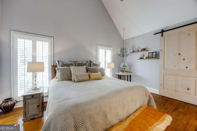 bedroom featuring a barn door, baseboards, high vaulted ceiling, and wood finished floors