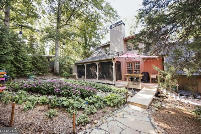 back of property featuring a deck, a chimney, and a sunroom