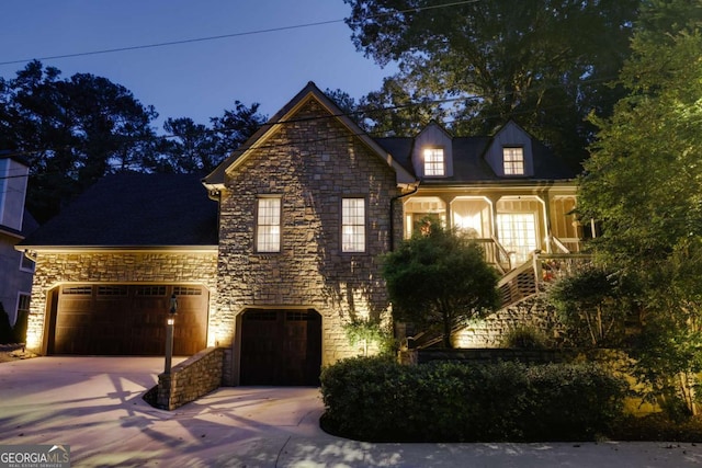 view of front of home with a porch, an attached garage, stone siding, and driveway