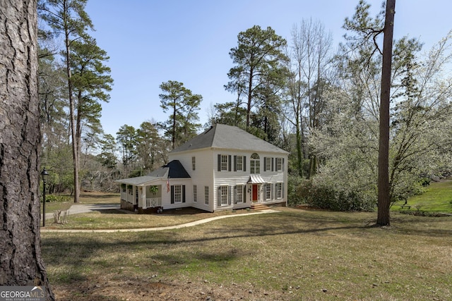 colonial-style house featuring a front yard and a shingled roof