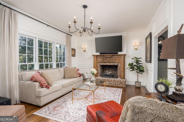 living area featuring a fireplace, wood-type flooring, crown molding, a decorative wall, and a notable chandelier