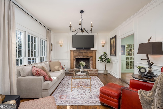 living area with ornamental molding, dark wood finished floors, an inviting chandelier, a decorative wall, and a brick fireplace