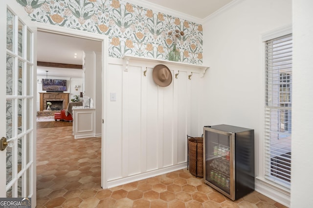 mudroom with a fireplace, beverage cooler, wallpapered walls, and ornamental molding