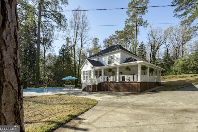 view of front of house with an outdoor pool, covered porch, driveway, and a chimney