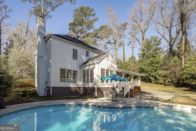 rear view of property with an outdoor pool, a patio, a chimney, and stairs