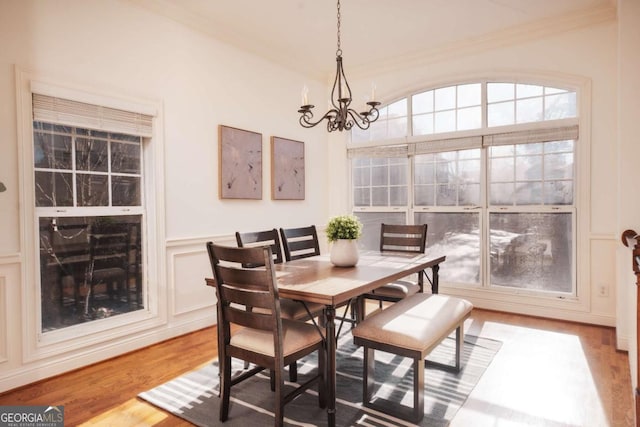 dining room featuring light wood-type flooring, a notable chandelier, crown molding, and a decorative wall