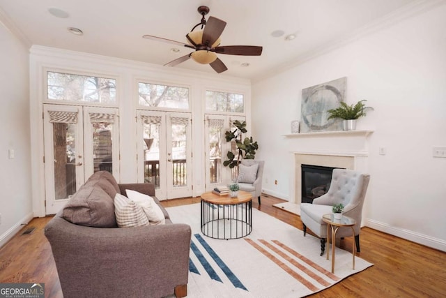 living room featuring wood finished floors, ceiling fan, ornamental molding, french doors, and a glass covered fireplace