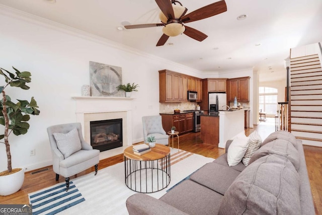 living area with visible vents, light wood-type flooring, a glass covered fireplace, and ornamental molding