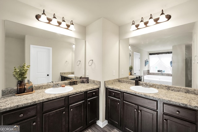 bathroom with a sink, wood finished floors, two vanities, and a bath