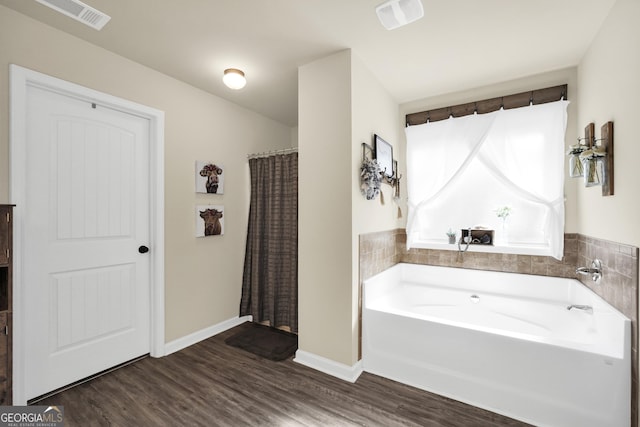 bathroom featuring a bath, wood finished floors, visible vents, and baseboards