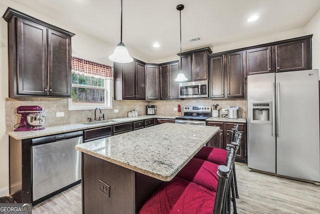 kitchen featuring a kitchen island, light wood-style flooring, a sink, stainless steel appliances, and dark brown cabinetry