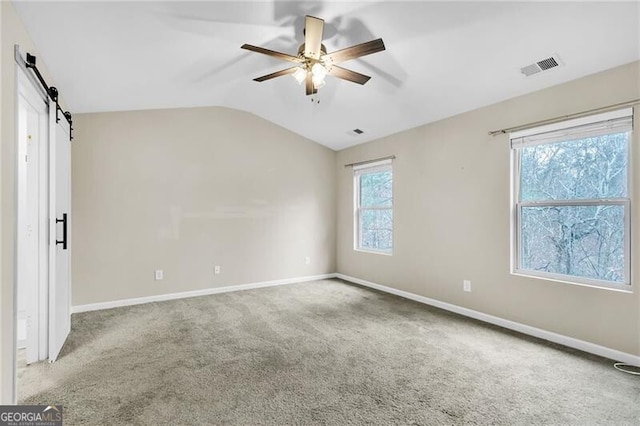 carpeted spare room featuring visible vents, a barn door, baseboards, ceiling fan, and vaulted ceiling