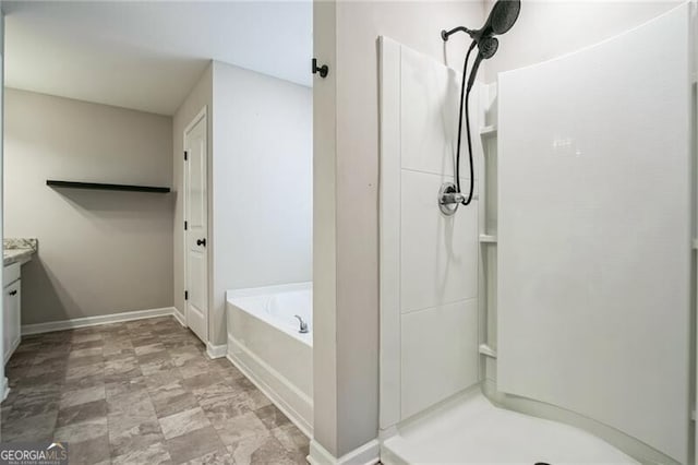 bathroom with a stall shower, baseboards, vanity, and a garden tub