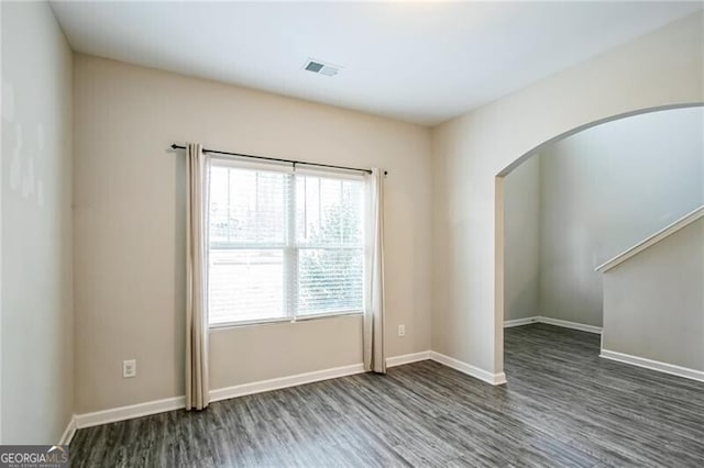 unfurnished room featuring visible vents, arched walkways, baseboards, and wood finished floors