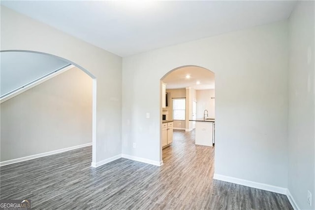 empty room featuring a sink, wood finished floors, baseboards, and arched walkways