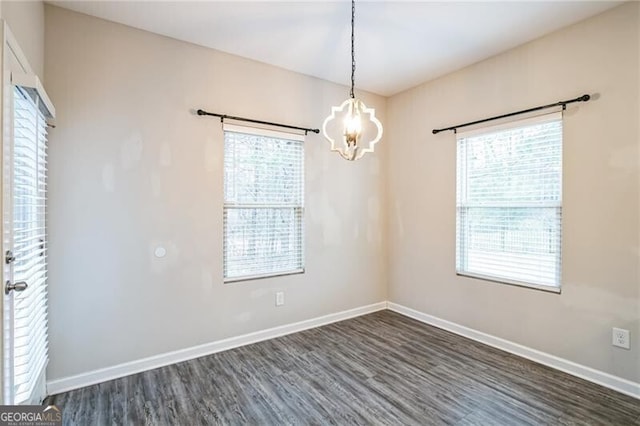 empty room featuring an inviting chandelier, dark wood-style floors, and baseboards