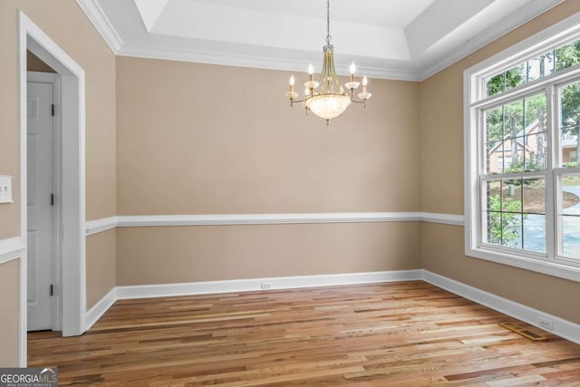 unfurnished room with a tray ceiling, a notable chandelier, light wood-style floors, and baseboards