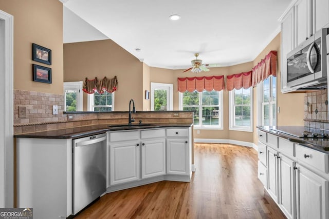 kitchen with a ceiling fan, a peninsula, a sink, appliances with stainless steel finishes, and dark countertops