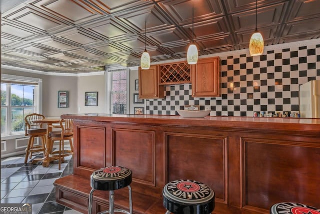 bar with dark tile patterned flooring, decorative light fixtures, an ornate ceiling, backsplash, and a community bar