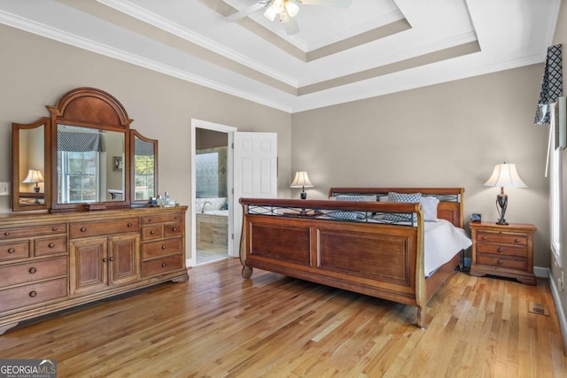 bedroom with crown molding, light wood-style flooring, a tray ceiling, and connected bathroom