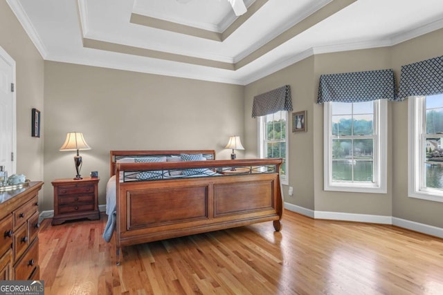 bedroom featuring a tray ceiling, baseboards, light wood-style flooring, and crown molding